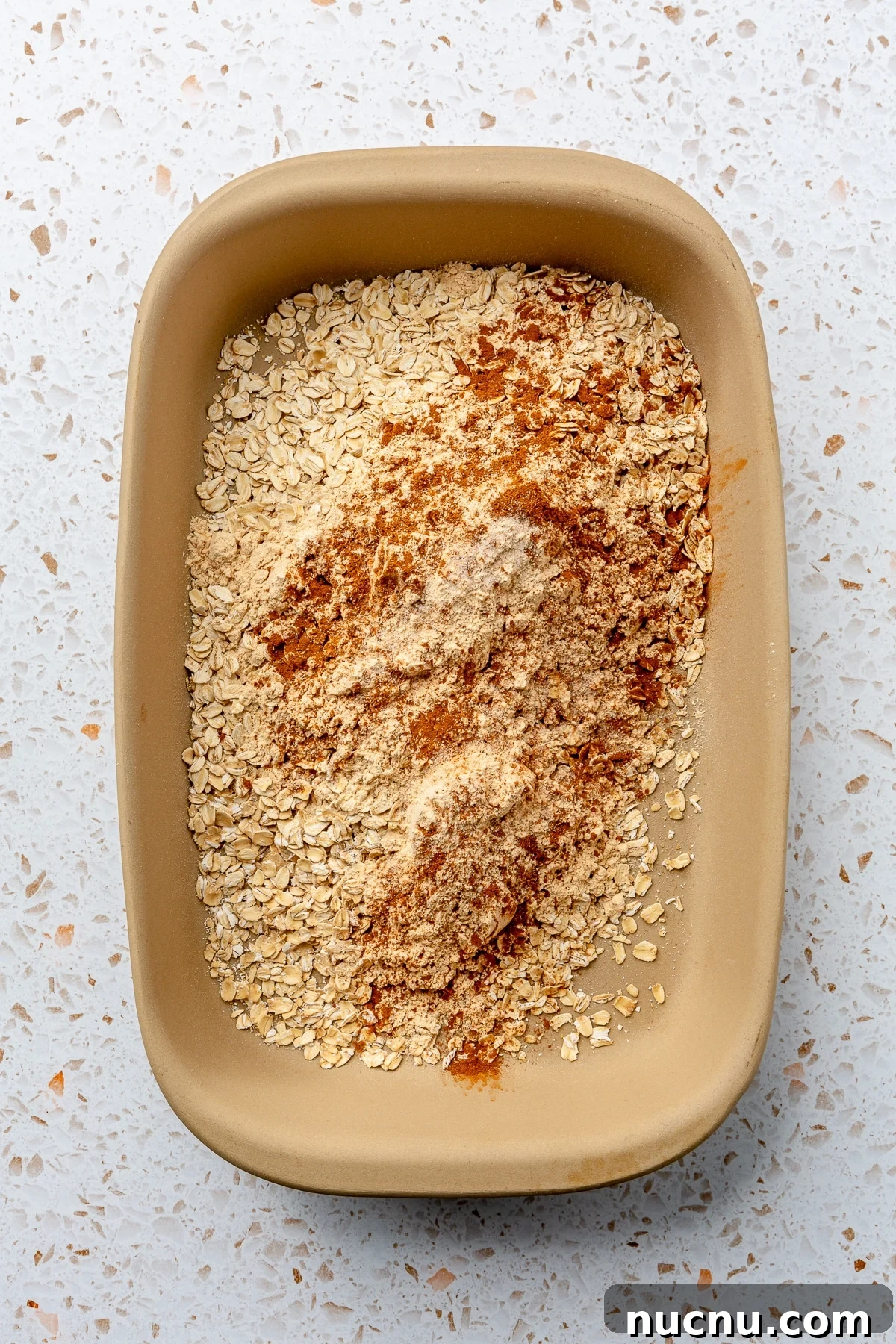A variety of dry ingredients have been added to a beige-colored baking dish.
