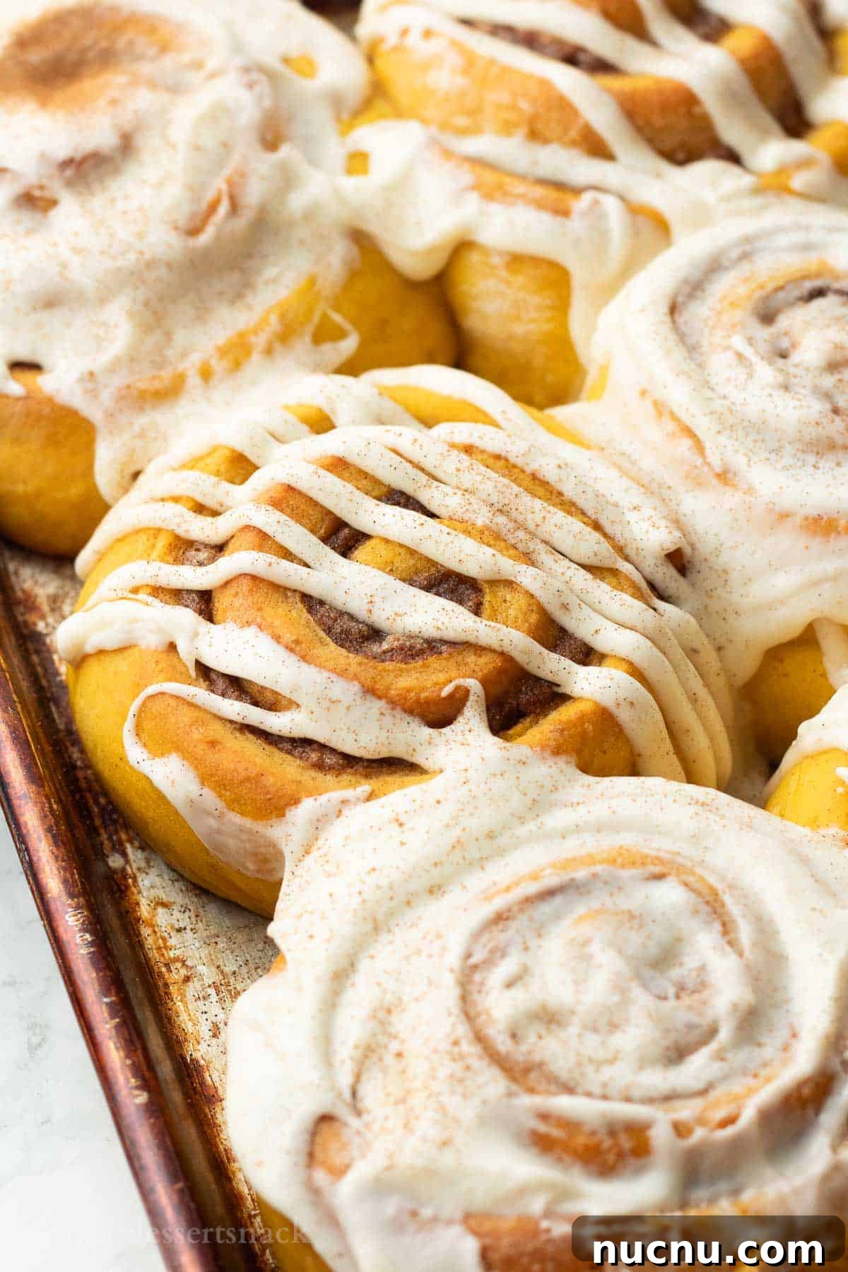 Pumpkin Spice Cinnamon Rolls: Soft, Fluffy Fall Recipe 2 Baked frosted pumpkin cinnamon rolls in metal pan.