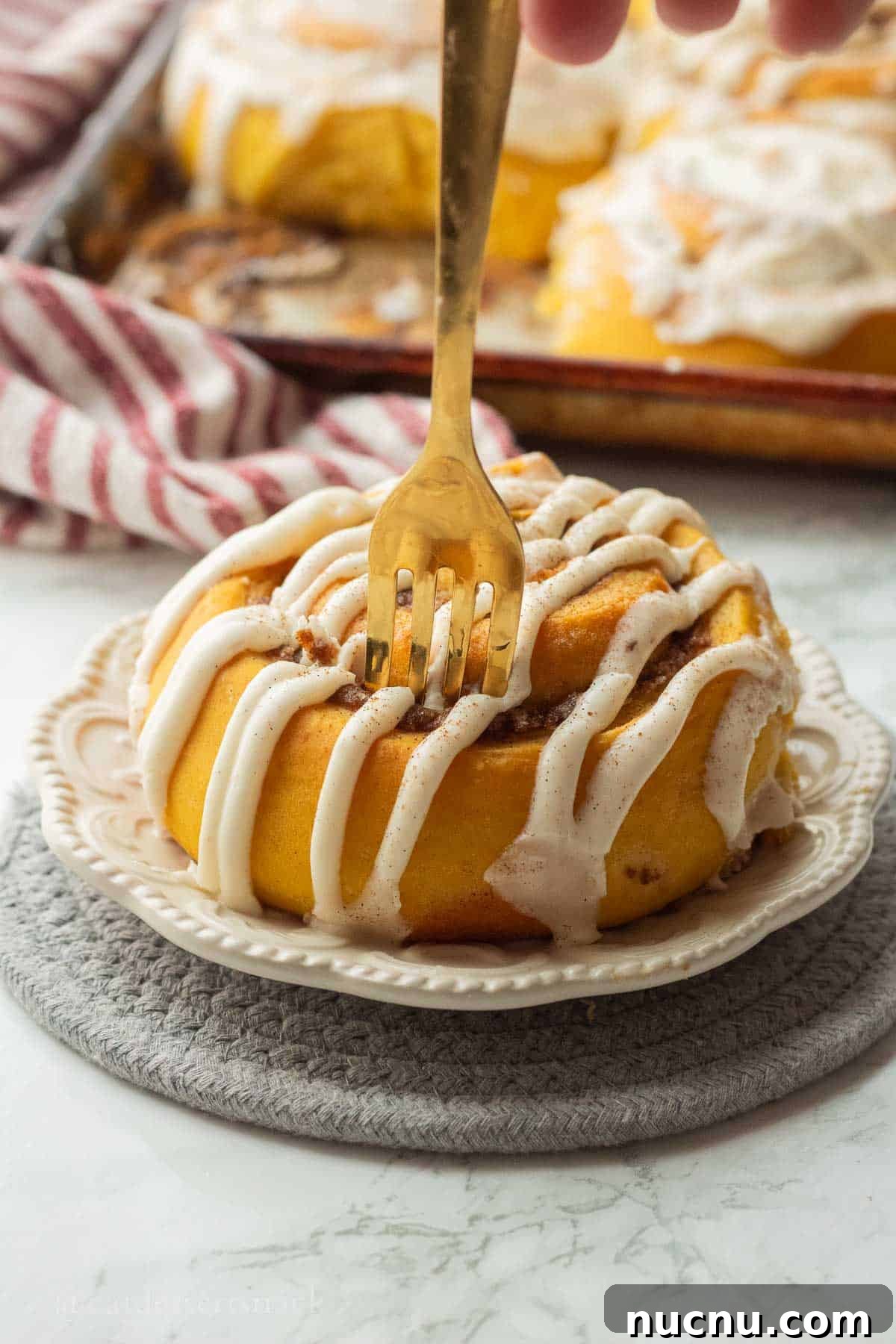 Pumpkin Spice Cinnamon Rolls: Soft, Fluffy Fall Recipe 12 Gold fork in iced pumpkin cinnamon roll on white plate.