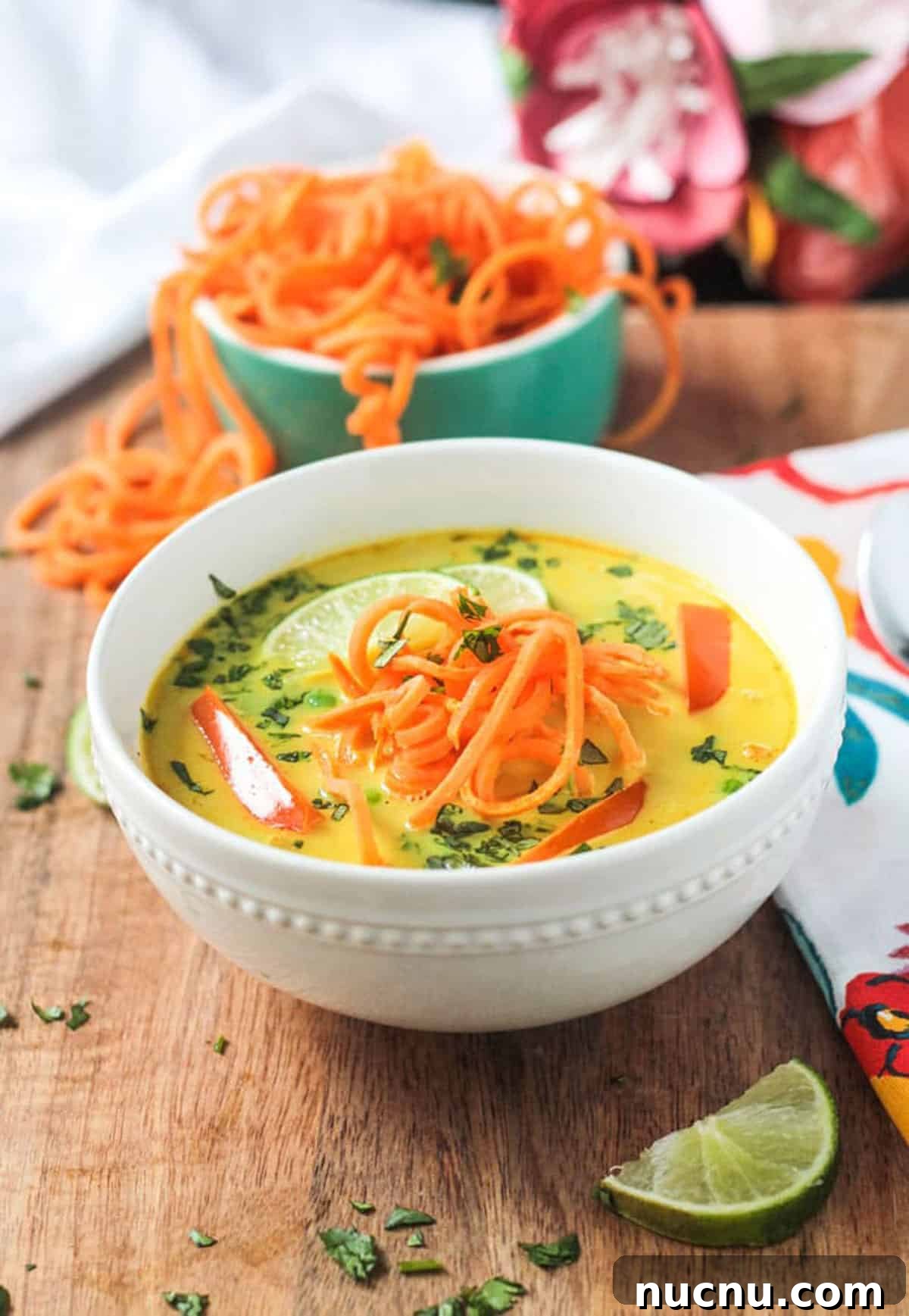 Coconut Curry Soup w/ Sweet Potato Noodles - Comforting and colorful dairy-free soup. Spiralized sweet potato noodles spilling out of a bowl behind a bowl of soup.