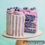 Classic Blueberry Cake Recipe: Moist, Fluffy, and Bursting with Fruit 10 A blueberry cake on a pedestal with a slice taken out showing layers of moist blueberry cake, blueberry buttercream, and blueberry compote filling.