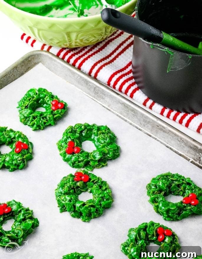 No-Bake Cornflake Christmas Wreath Treats 4 christmas cornflake wreath cookies with red candies on parchment paper