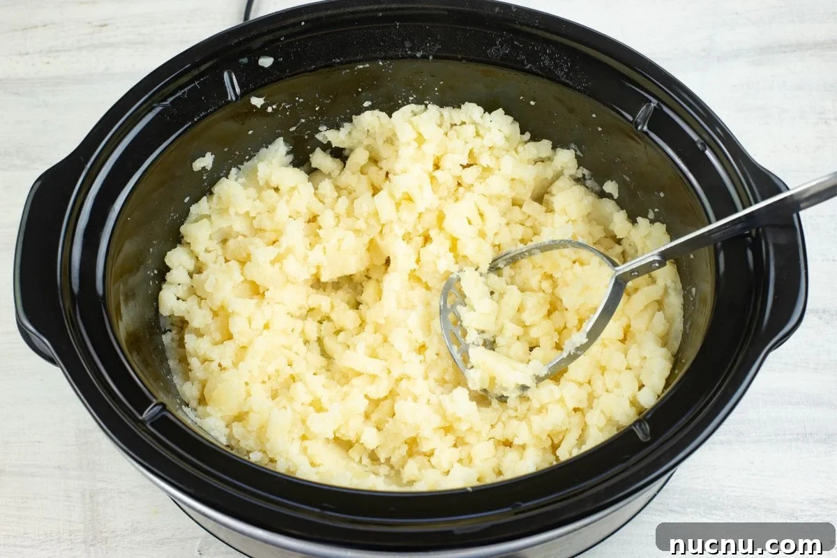 Million-Dollar Slow Cooker Mashed Potatoes Recipe 5 Mashing cooked potatoes in a warm slow cooker.