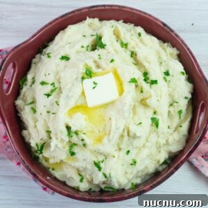 Million-Dollar Slow Cooker Mashed Potatoes Recipe 10 Serving bowl filled with Million Dollar Mashed Potatoes garnished with parsley.
