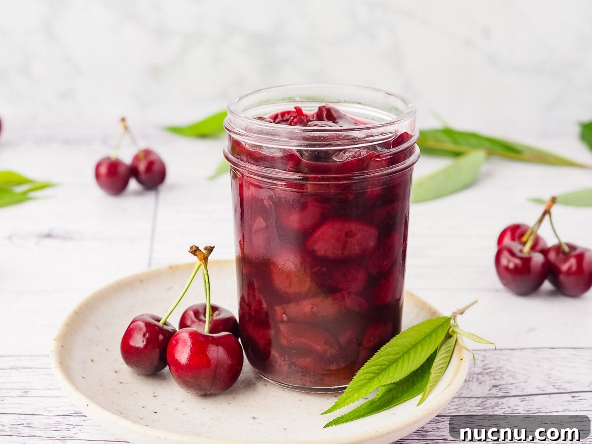 Homemade Cherry Compote Recipe for Desserts and Breakfast 2 Compote in a mason jar on a plate, with fresh cherries and leaves.