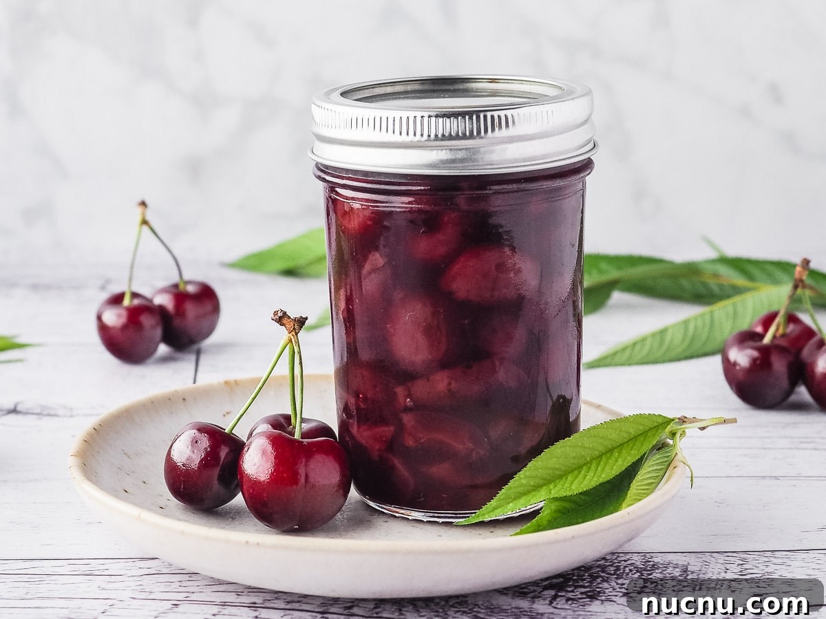 Homemade Cherry Compote Recipe for Desserts and Breakfast 7 Compote in a mason jar on a plate, with fresh cherries and leaves.