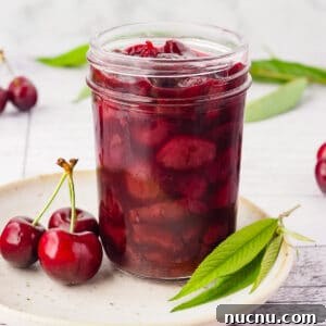Homemade Cherry Compote Recipe for Desserts and Breakfast 8 Close up compote in a mason jar on a plate, with fresh cherries and leaves.