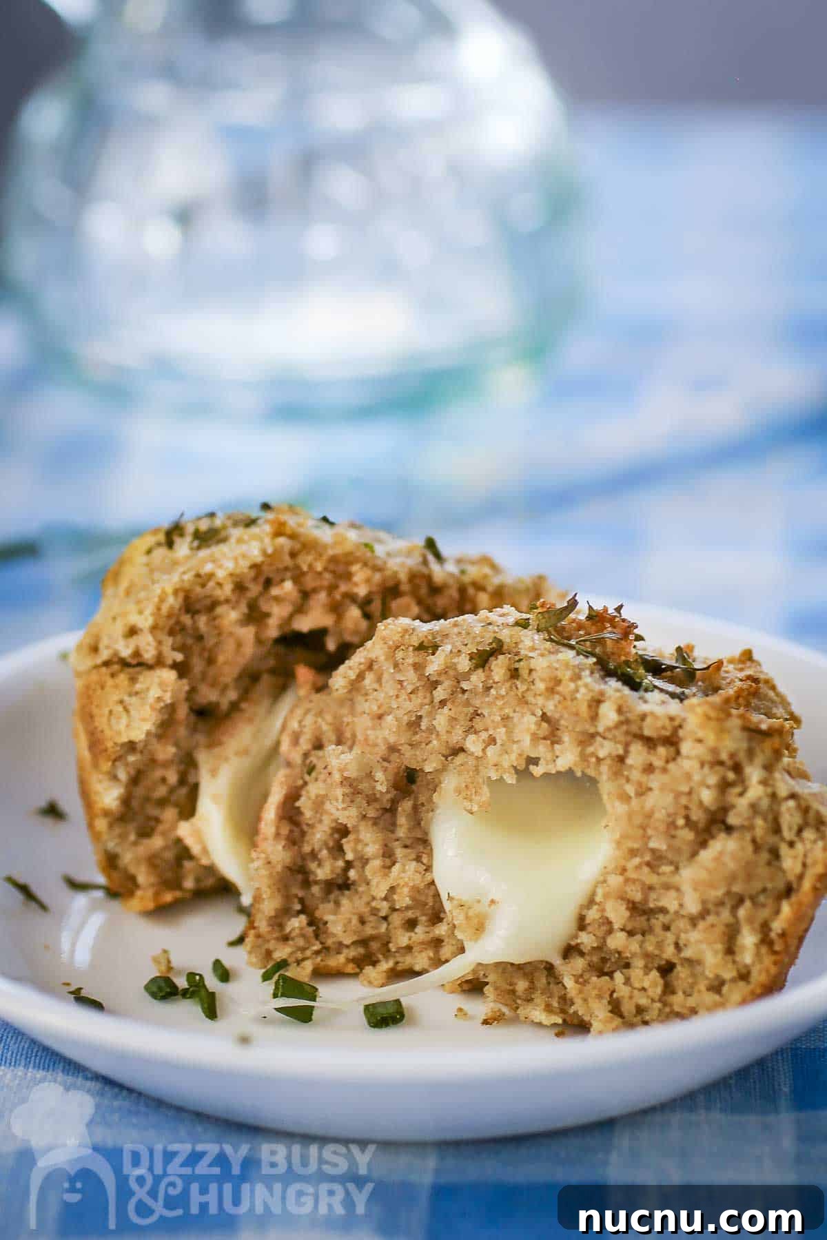 Side shot of a biscuit split in half with mozzarella inside garnished with fresh herbs on a white plate.