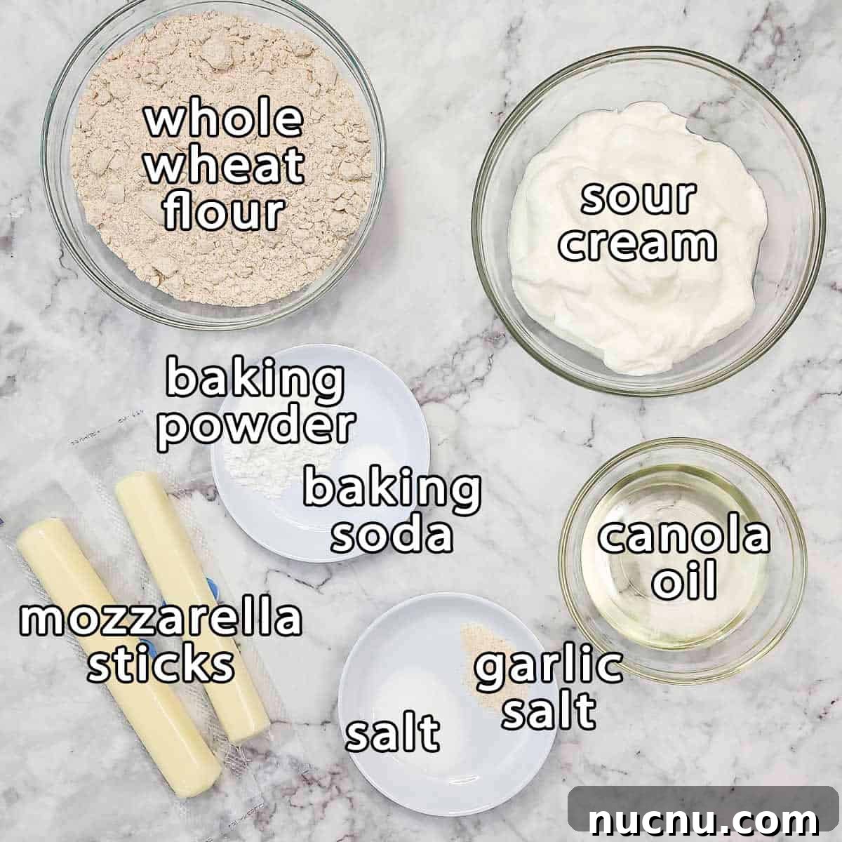 Overhead shot of ingredients - whole wheat flour, sour cream, baking powder, baking soda, canola oil, mozzarella sticks, salt and garlic salt.