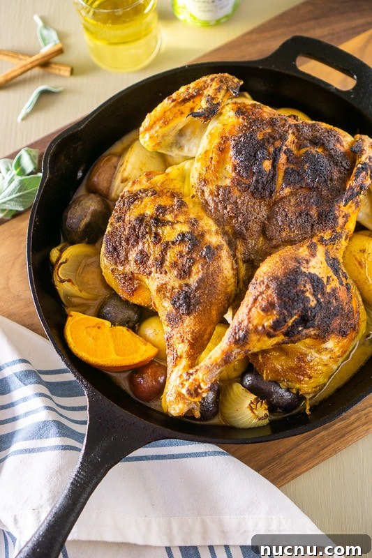 Spatchcock Chicken Roasted with Apple Cider Glaze 5 Cast iron skillet containing a roasted apple cider spatchcock chicken with orange and potatoes.