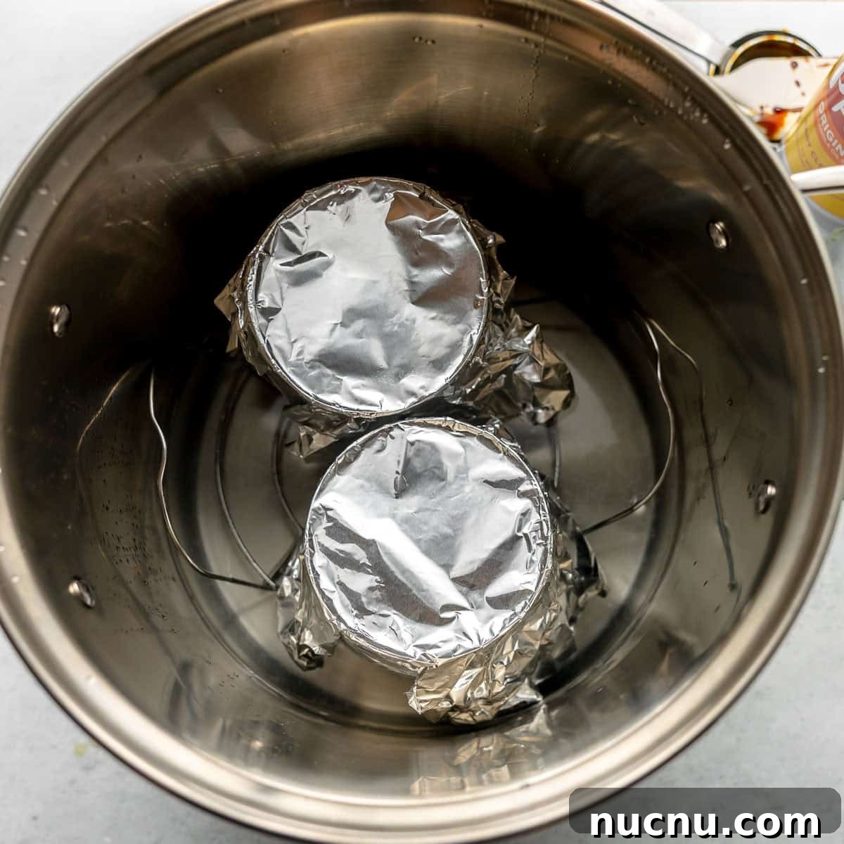 Authentic Boston Brown Bread Recipe: Steamed New England Classic 12 Two cans covered with aluminum foil sit on a rack inside a large stainless steel pot, prepared for a water bath.