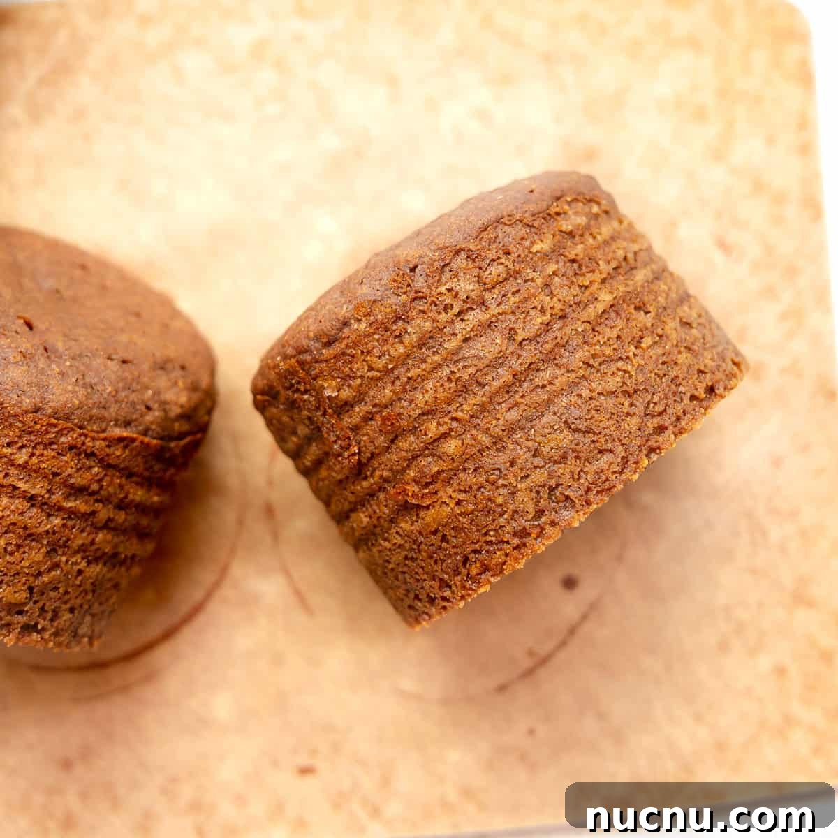 Authentic Boston Brown Bread Recipe: Steamed New England Classic 13 Two brown, round baked goods with textured sides, placed on a light brown surface.