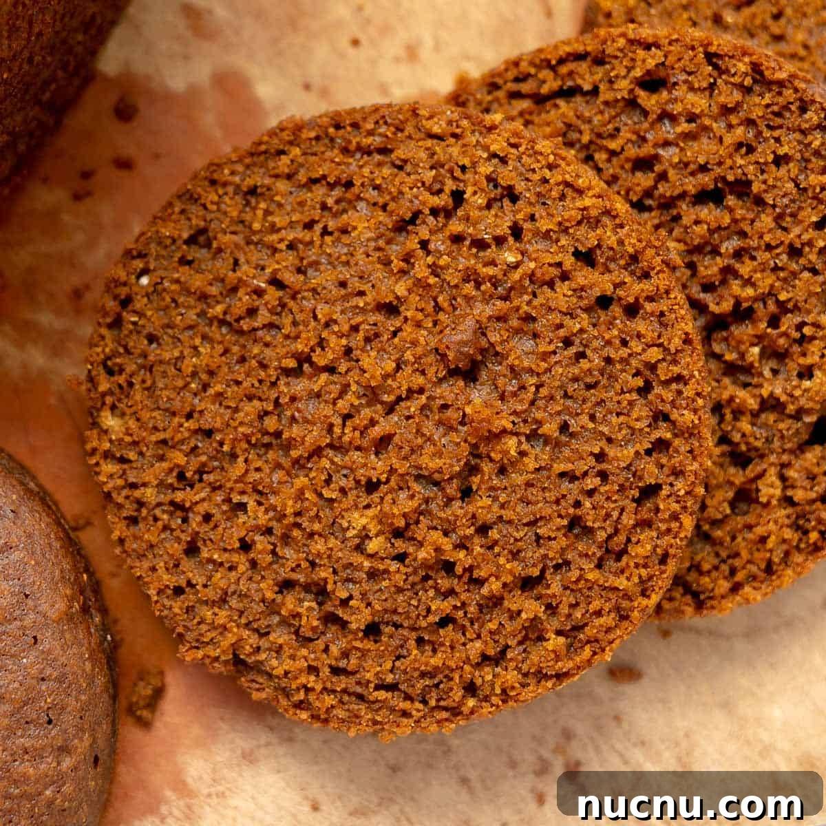Authentic Boston Brown Bread Recipe: Steamed New England Classic 14 Two slices of dark brown bread lie on parchment paper, showing a moist and slightly crumbly texture.