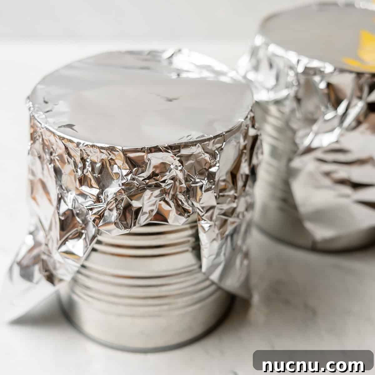 Authentic Boston Brown Bread Recipe: Steamed New England Classic 4 Two metal cans are covered with aluminum foil, sitting on a white surface.
