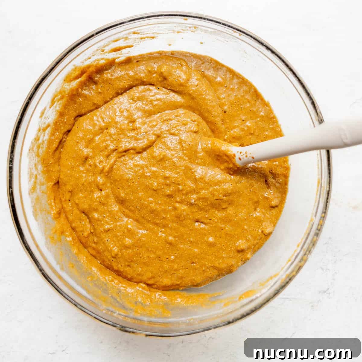 Authentic Boston Brown Bread Recipe: Steamed New England Classic 9 A glass bowl filled with brown bread batter and a white spatula resting inside on a white surface.