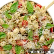 Chicken pesto pasta salad in a white serving bowl with serving spoon.