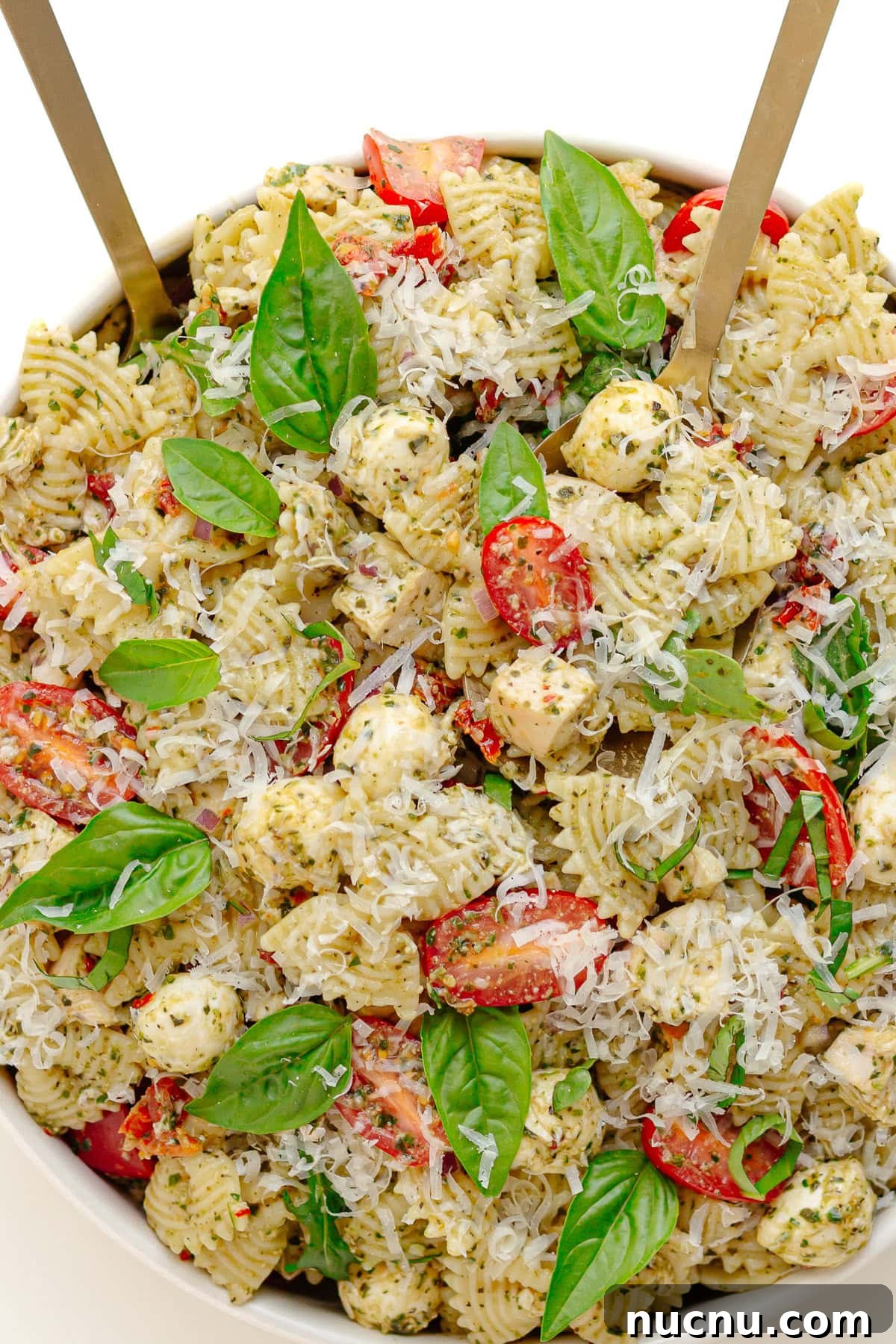 Creamy Chicken Pesto Pasta Salad with Sun-Dried Tomatoes 6 White serving bowl of pesto chicken pasta salad with two salad servers sticking out.