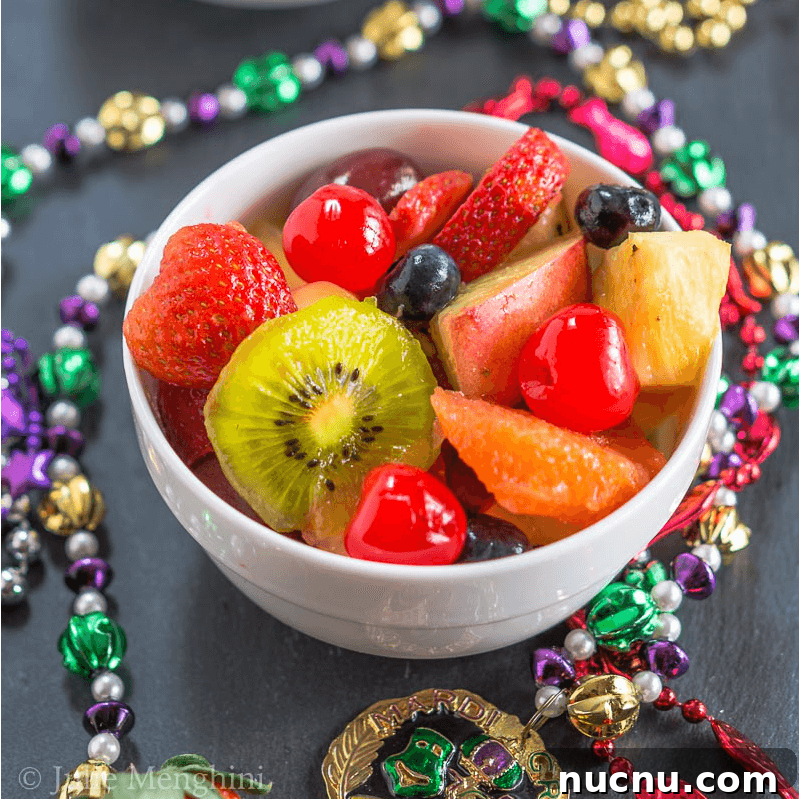 Boozy Mardi Gras Fruit Salad Recipe for Festive Parties 2 A white bowl filled with rum marinated Hurricane chunks of fresh fruit for Mardi Gras and surrounded by colorful beads.