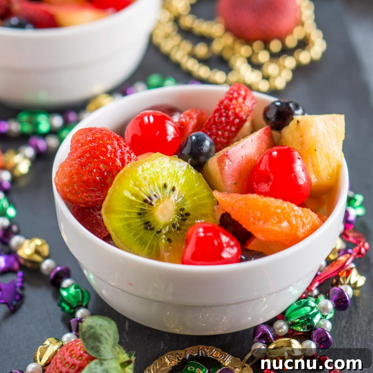 Boozy Mardi Gras Fruit Salad Recipe for Festive Parties 6 A white bowl filled with chunks of fresh fruit and surrounded by colorful beads.